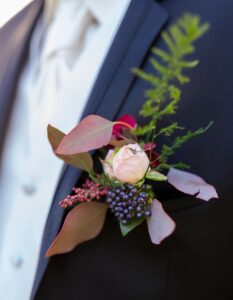 Boutonière du mariée avec rose pastel, asparagus, ecaliptus, baies rouges et violette foncée