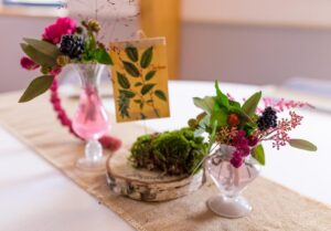 Chemin de table mariage avec rondin de boulot et deux vases en verre contenant des murs et d'autre baies, des amarantes et du feuillage vert.