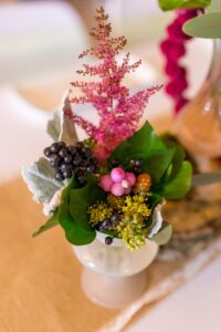 Petit vase pour chemin de table contenant du feuillage, des baies roses et noirs et une graminée rose