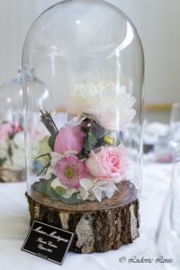 Des roses et des pivoines blanches sous cloche et des rondins de bois pour une décoration de mariage romantique