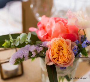 Petit centre de table constituée de pivoine corail de rose pastel et de pois de senteur et de bleuet dans un bocal en verre