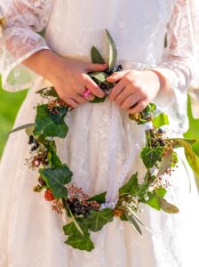 Couronne végétative de demoiselle d'honneur avec lierre, eucaliptus, gypsophile, mures et baies noires portée entre les mains d'une petite filles